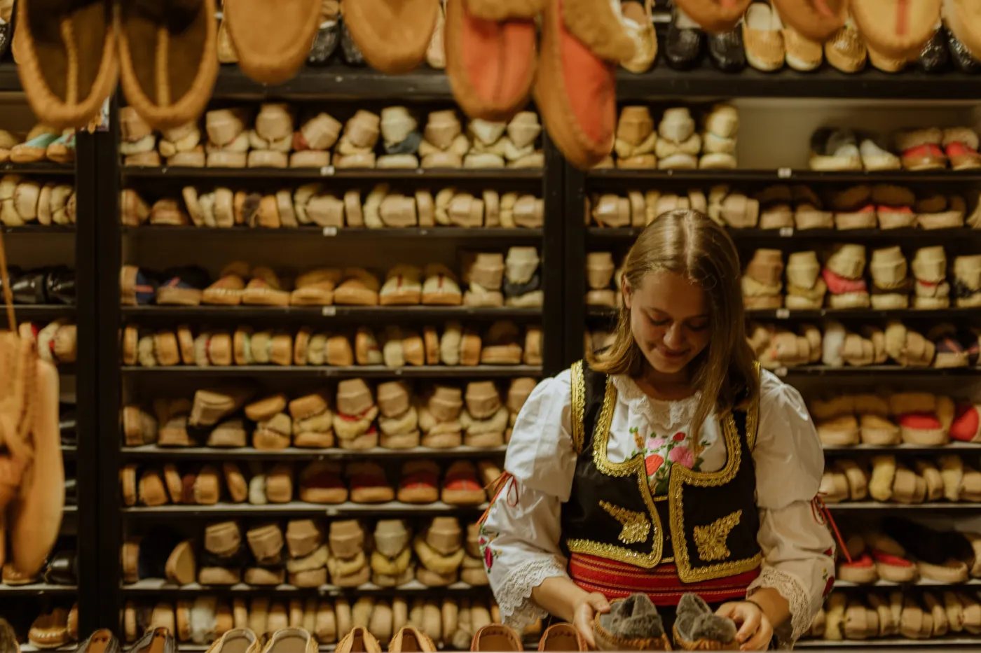A woman in Serbian traditional dress surrounded by handmade Opanak Strugarević footwear